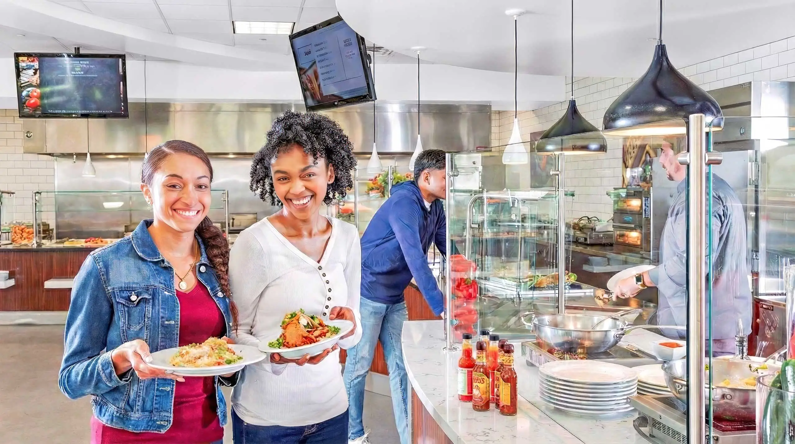 Two students happily holding plates of food in the middle of serving area